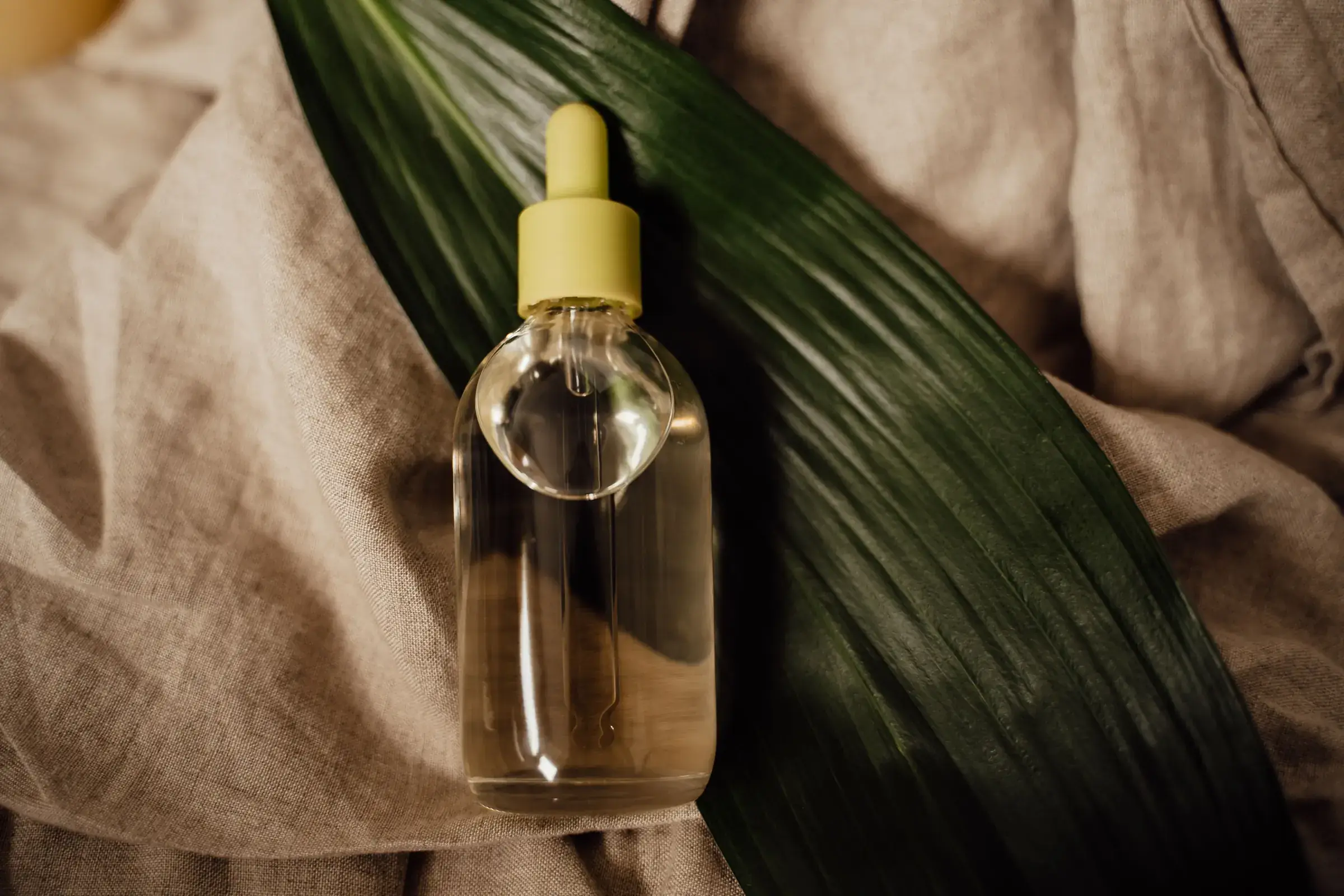 Flacon de sérum posé sur une feuille verte et un lin beige